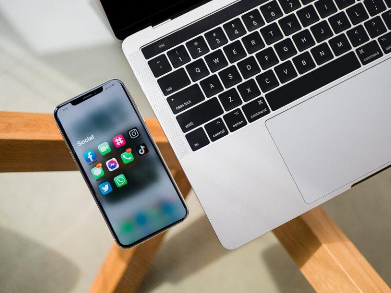 Smartphone con app social accanto a laptop, confronto tra social media e sito web per il business online